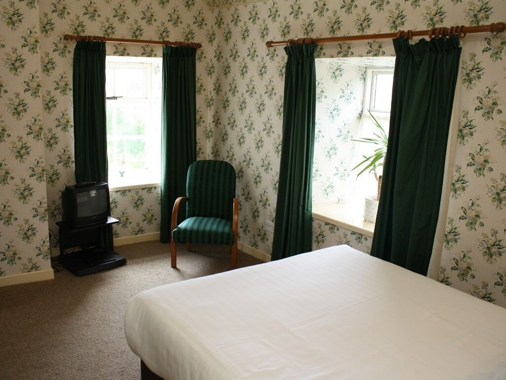 A hotel room with a bed, a chair, a television, and windows with curtains.