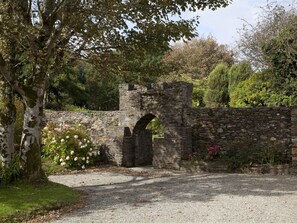 A stone archway leading into a garden with white roses and a tree. - Woodhill House (Ardara)