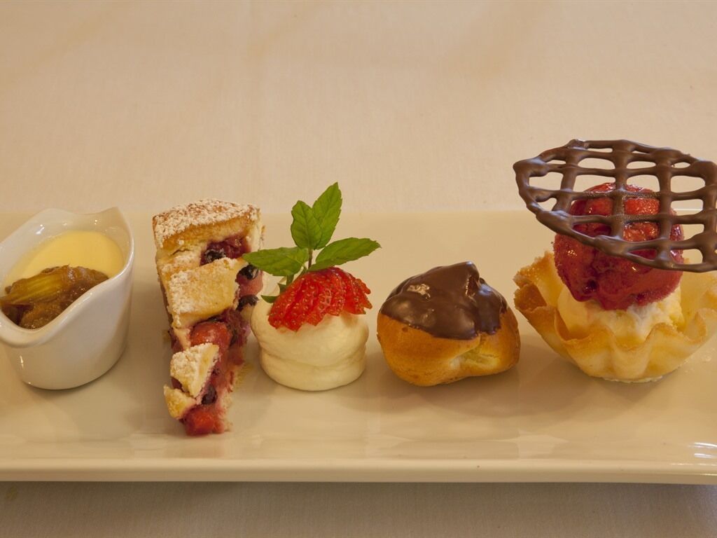 A dessert tray with various pastries and a small bowl of sauce.