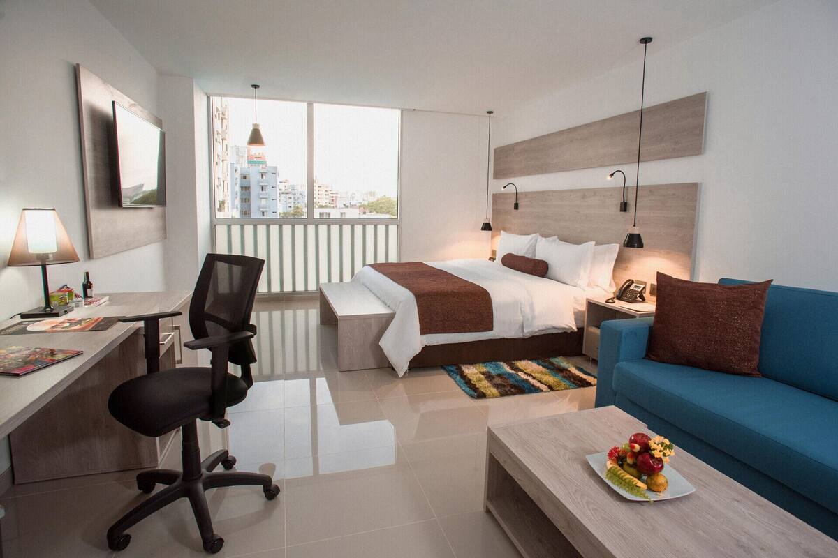 Ein modernes Hotelzimmer mit Bett, Schreibtisch, Sessel, Sofa und Blick auf die Stadt.