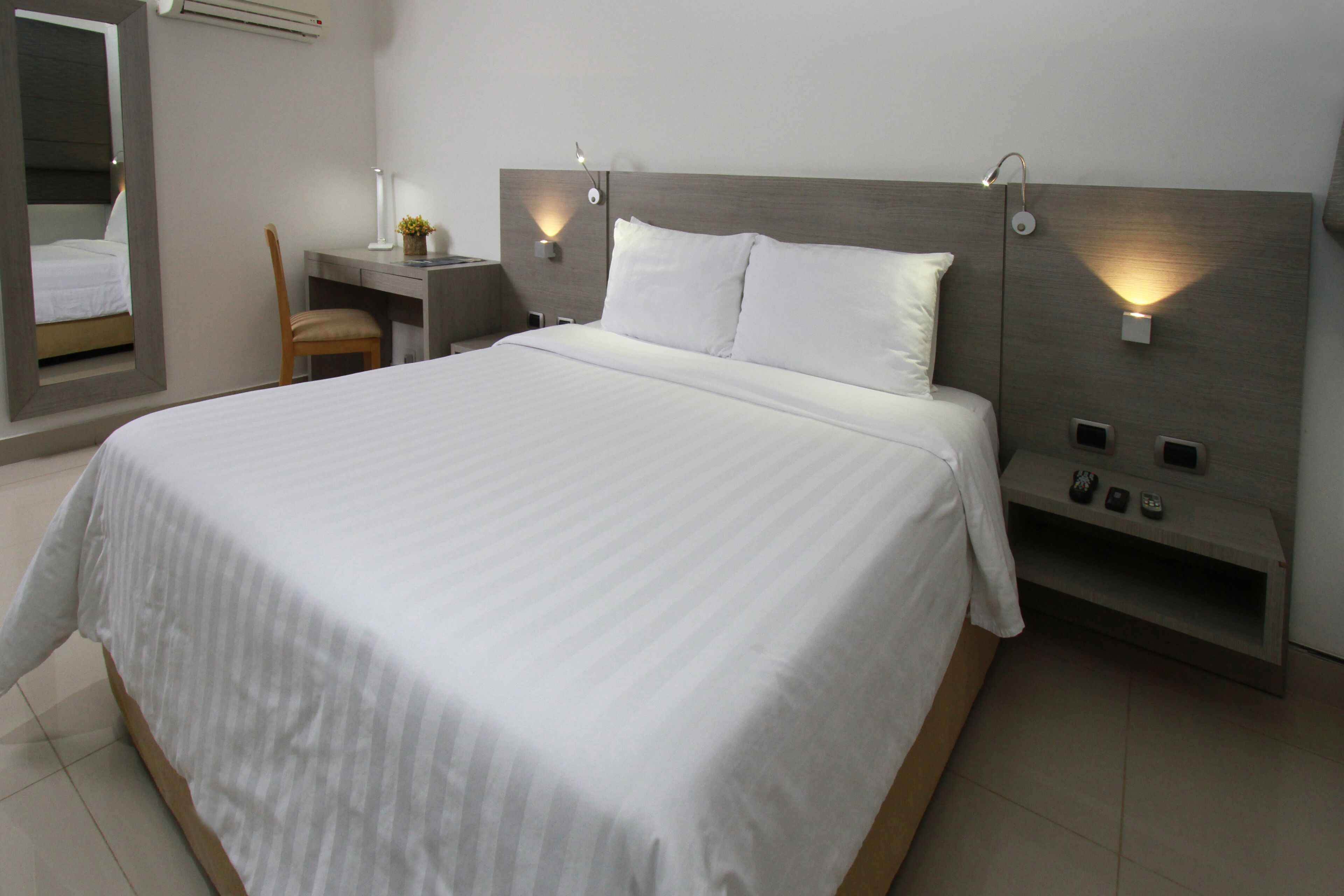 A modern hotel room with a large bed, a desk, a chair, and a mirror.