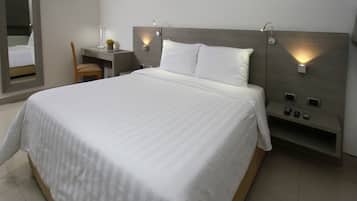 A modern hotel room with a large bed, a desk, a chair, and a mirror.