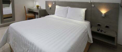 A modern hotel room with a large bed, a desk, a chair, and a mirror.