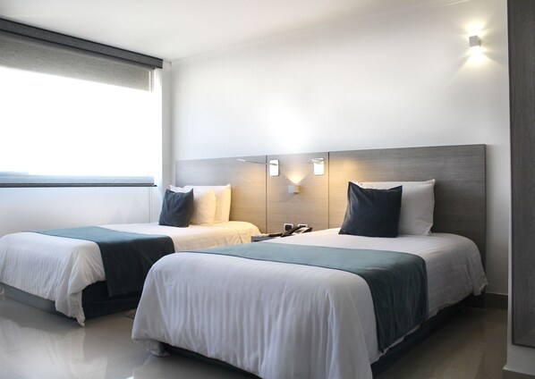 A modern hotel room with two beds, a large window, and a wall-mounted light fixture.