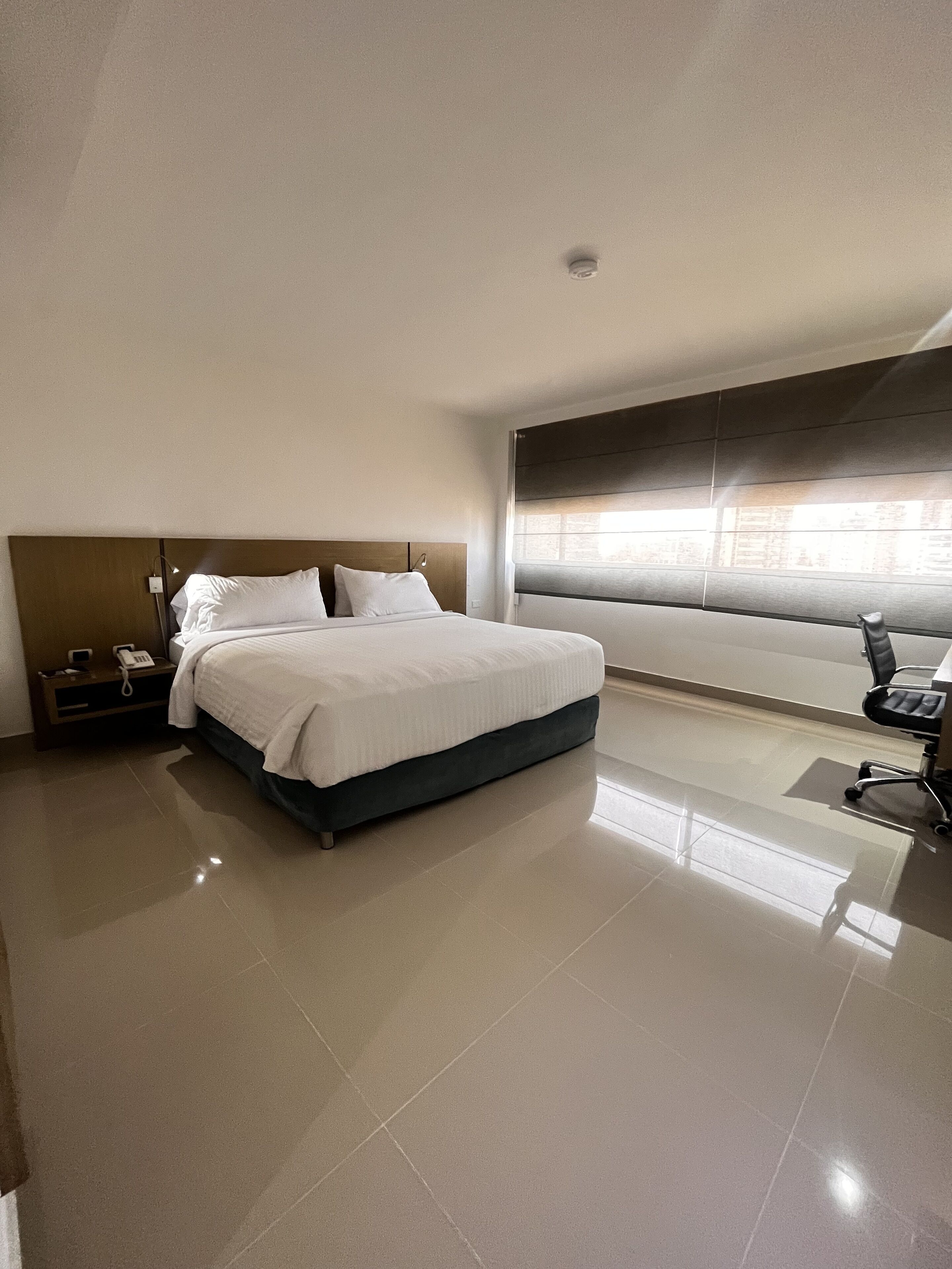 Una habitación de hotel moderna con una cama grande, una mesita de noche con un teléfono y una silla.