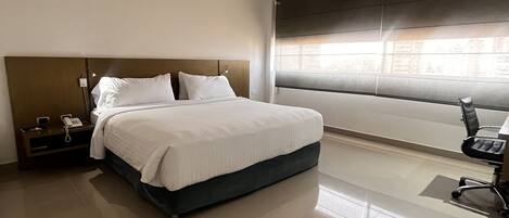 Una habitación de hotel moderna con una cama grande, una mesita de noche con un teléfono y una silla.