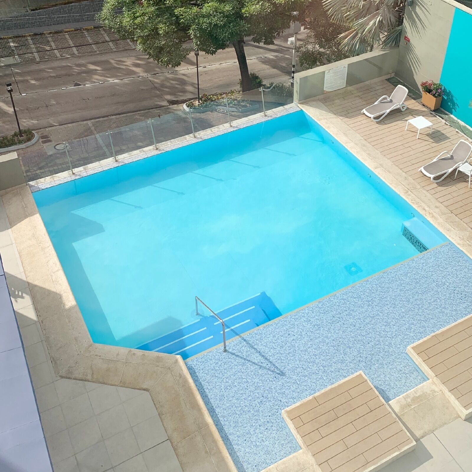 A rectangular swimming pool with a blue interior, surrounded by a tiled deck. There are lounge chairs and a small planter with flowers.