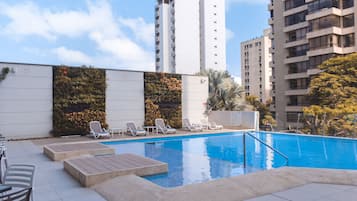 Una piscina en la azotea con sillones de descanso y vistas a edificios altos.