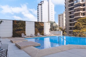 Una piscina en la azotea con sillones de descanso y vistas a edificios altos.