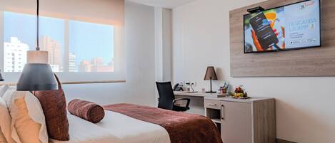 A modern hotel room with a bed, desk, and a large TV screen displaying an app download advertisement.