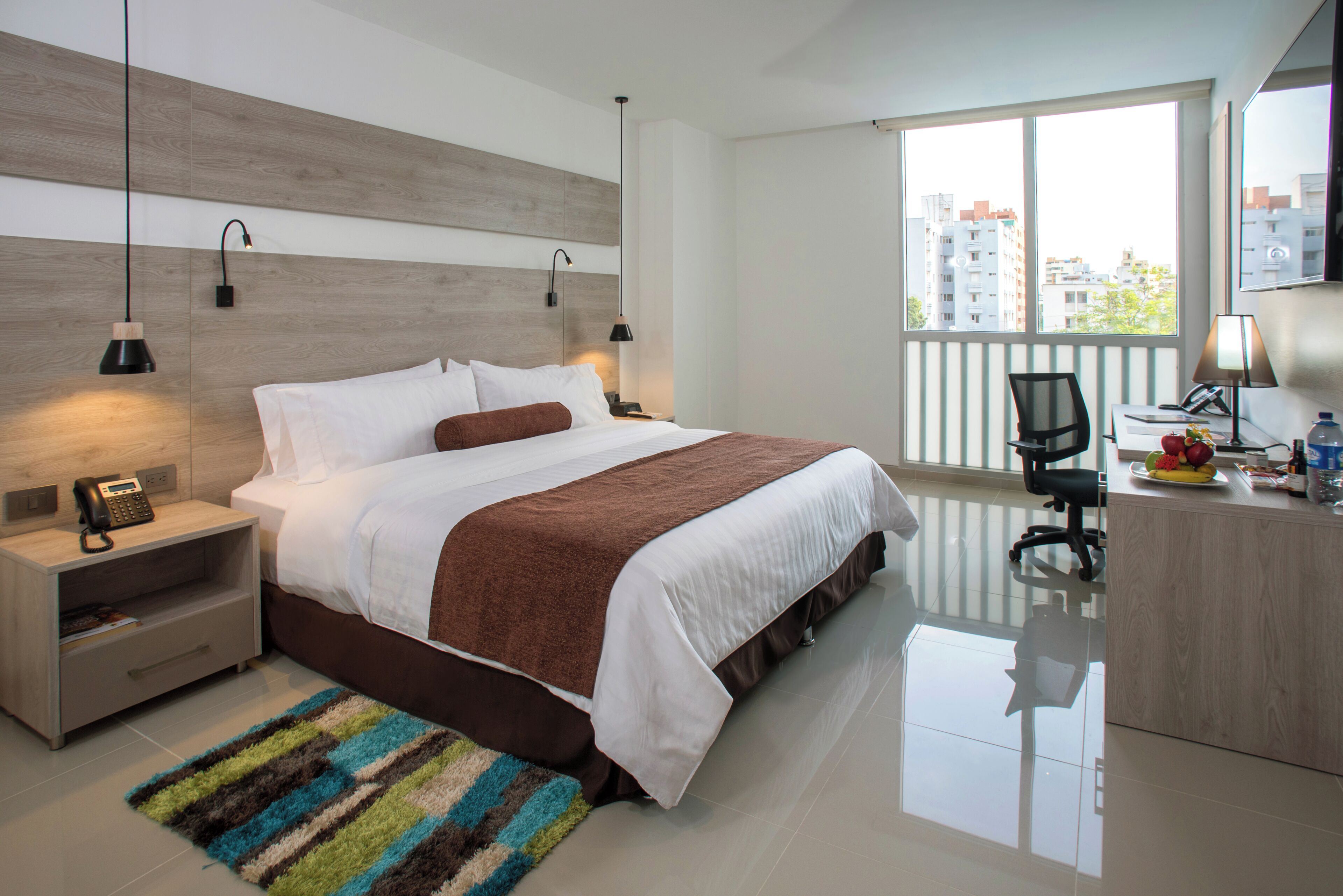 Een moderne hotelkamer met een groot bed, nachtkastjes, een bureau en uitzicht op de stad.