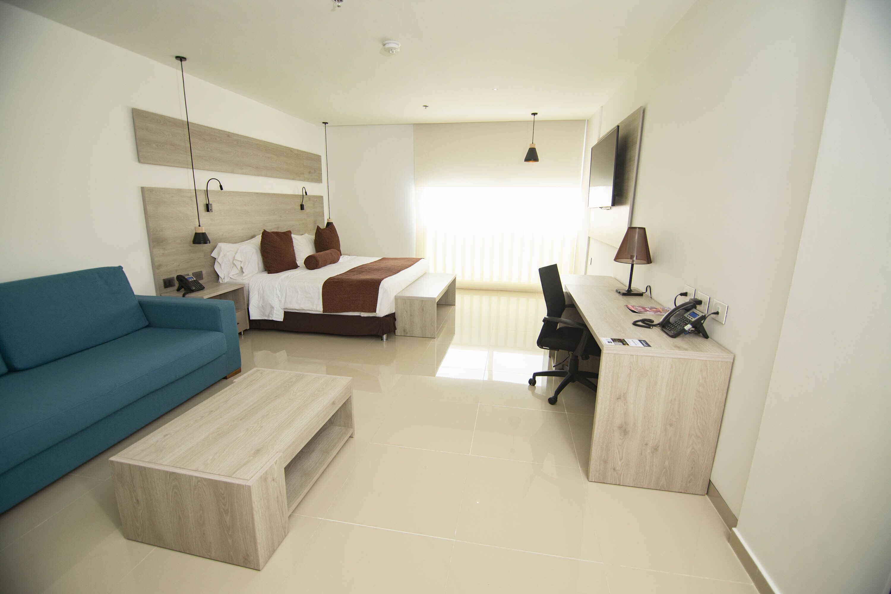 A modern hotel room with a bed, a blue sofa, a wooden desk, and a television.