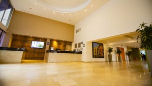Eine geräumige Lobby mit einer Rezeption, einem großen Gemälde und Zimmerpflanzen.