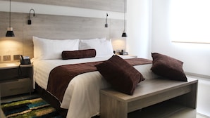 Ein modernes Schlafzimmer mit einem Holzkopfende, einem großen Bett mit weißer und brauner Bettwäsche, zwei Nachttischen mit Lampen und einem farbenfrohen Teppich.