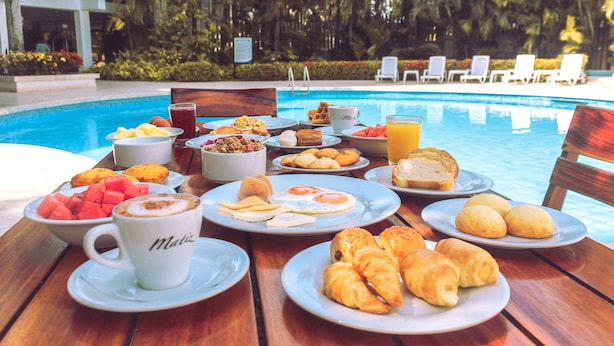 Ein Frühstücksbuffet am Pool mit verschiedenen Speisen und einer mit 'Mali' beschrifteten Kaffeetasse.