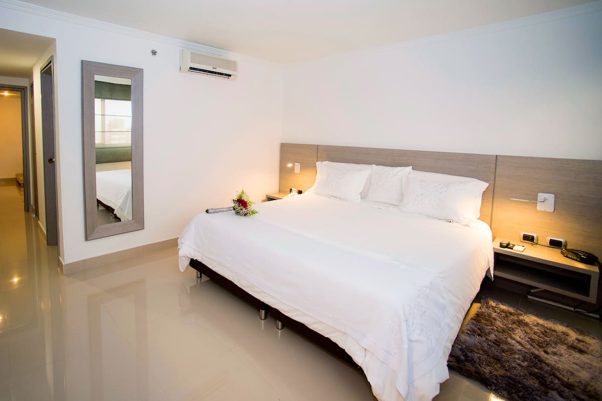 Ein modernes Hotelzimmer mit einem großen Bett, Nachttischen, einem Spiegel und einer Klimaanlage.