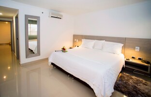 A modern hotel room with a large bed, bedside tables, a mirror, and an air conditioning unit.
