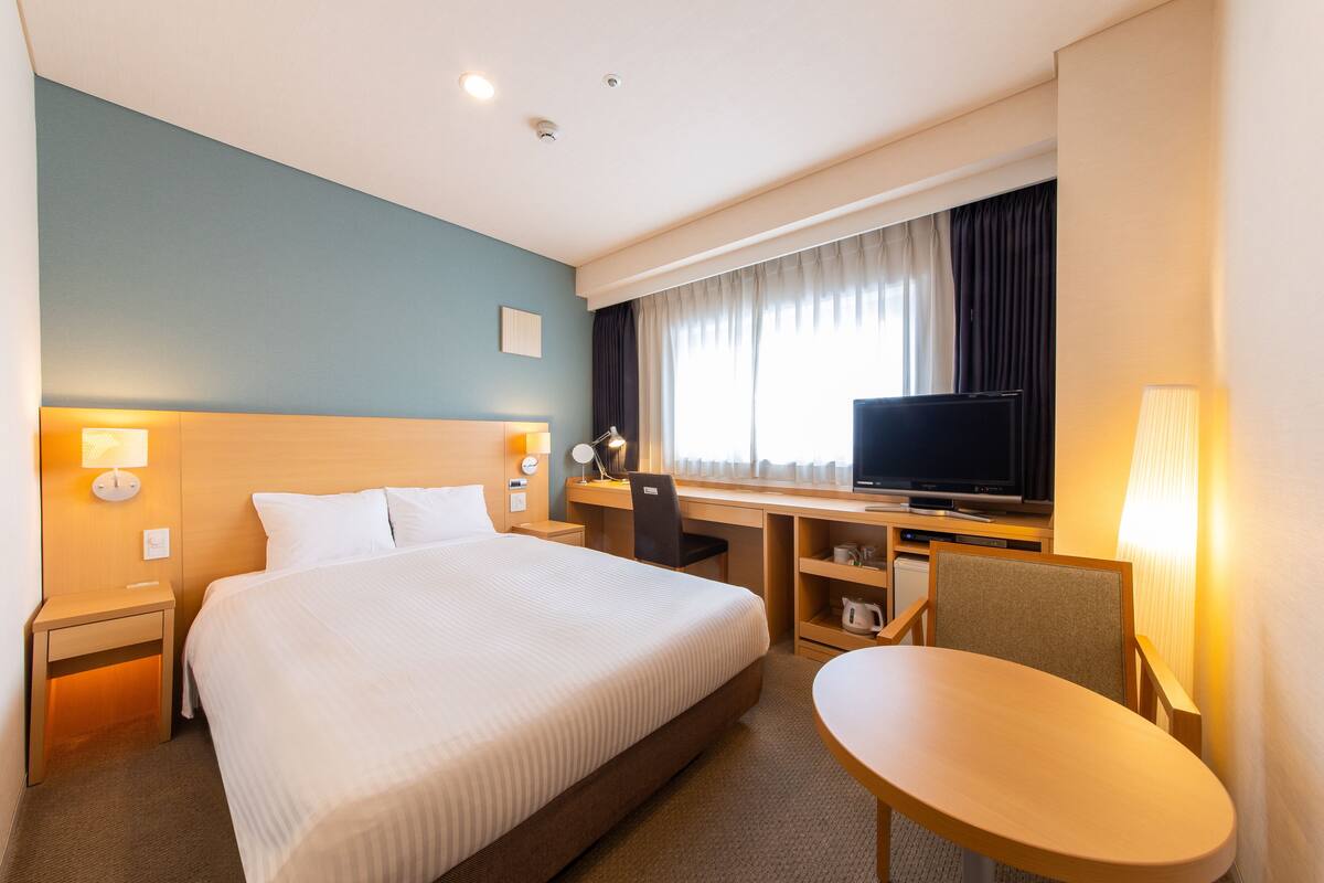 A hotel room with a large bed, a desk with a chair, a television, and a small table.