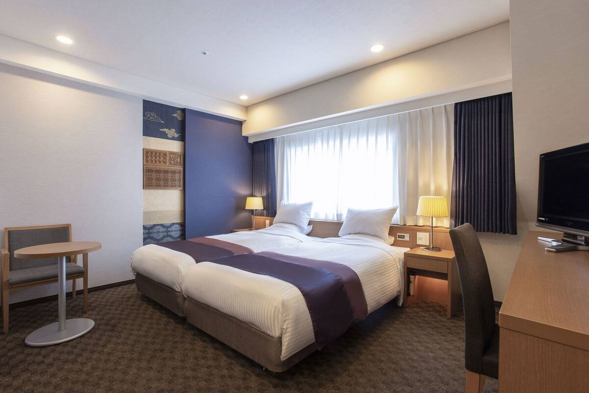 A hotel room with a large bed, a desk with a computer, a chair, and a TV.