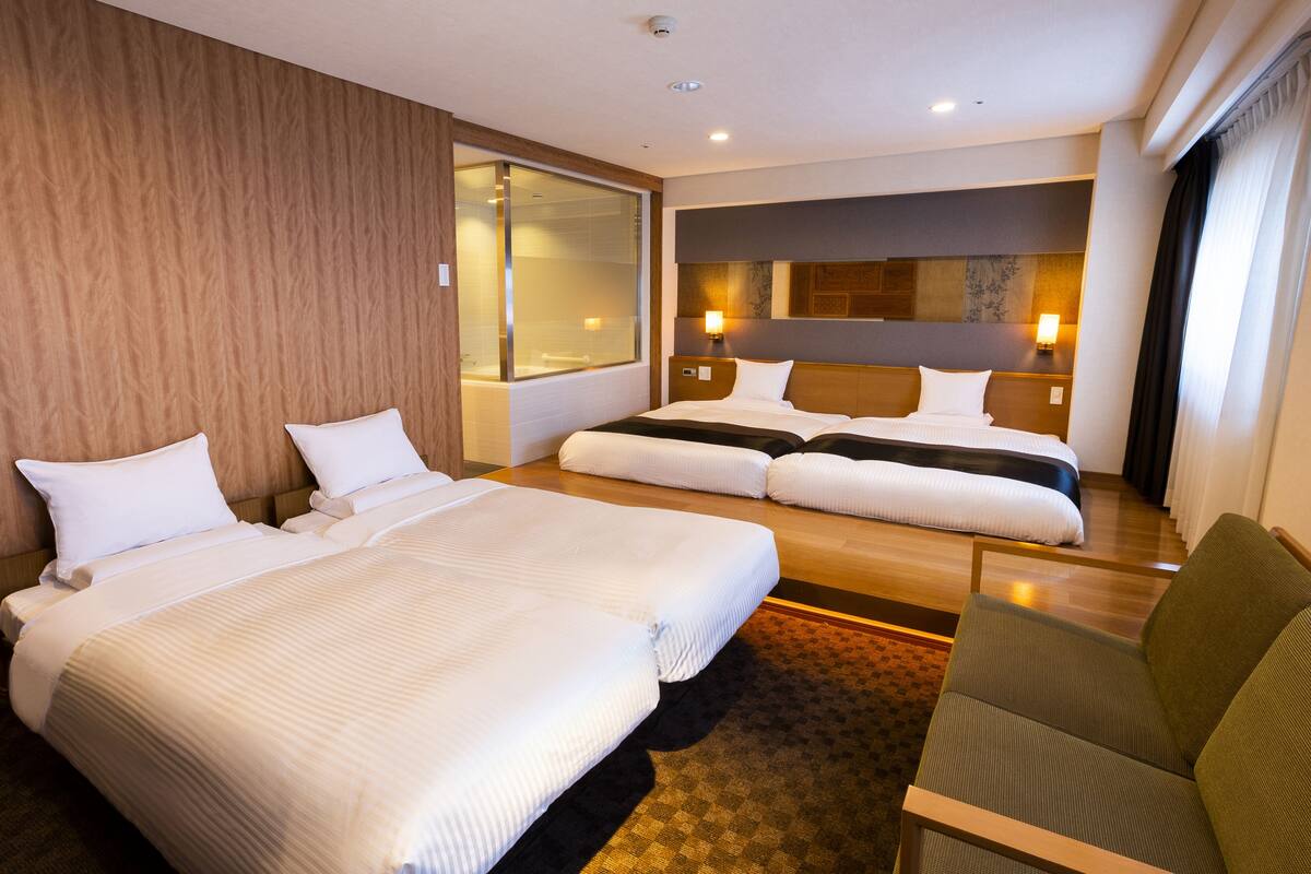 A hotel room with two large beds, a sofa, a large window, and a mirror.