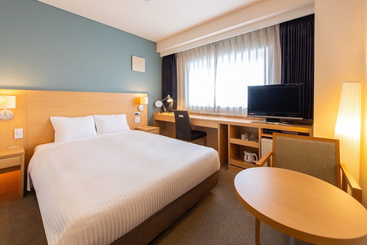 A hotel room with a bed, desk, TV, chair, and lamp.