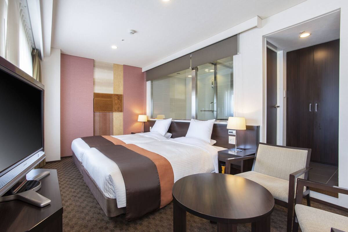 A hotel room with a large bed, a TV, a desk with a lamp, and a chair.