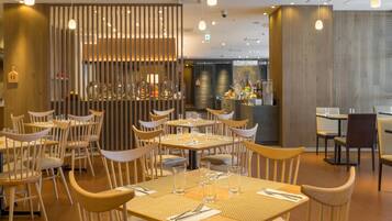Een modern restaurantinterieur met houten meubels, hanglampen en een bar in het midden.