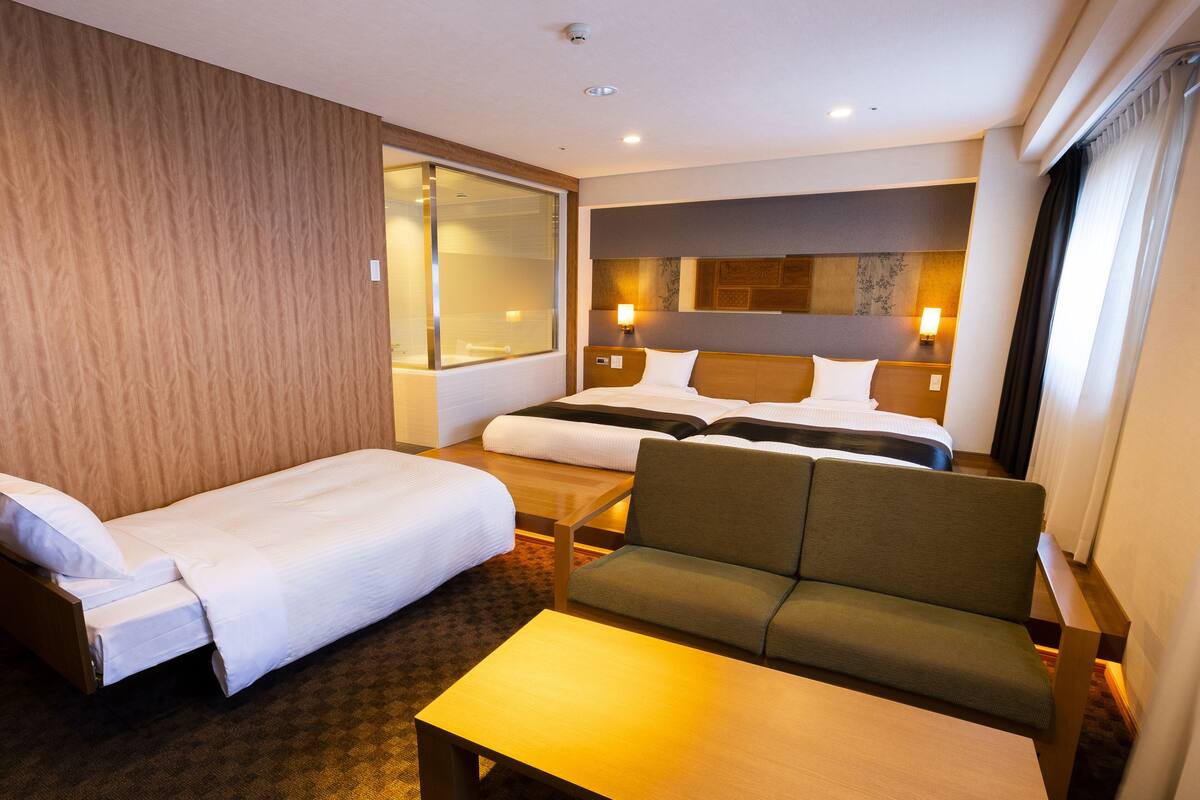 A hotel room with a bed, a sofa, a small table, and a large window.