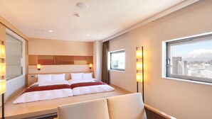 Habitación de hotel con cama, una silla, ventanal con vista a la ciudad y una lámpara de pared.