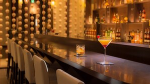 Una zona de bar con una barra larga, taburetes y una variedad de botellas en estanterías.