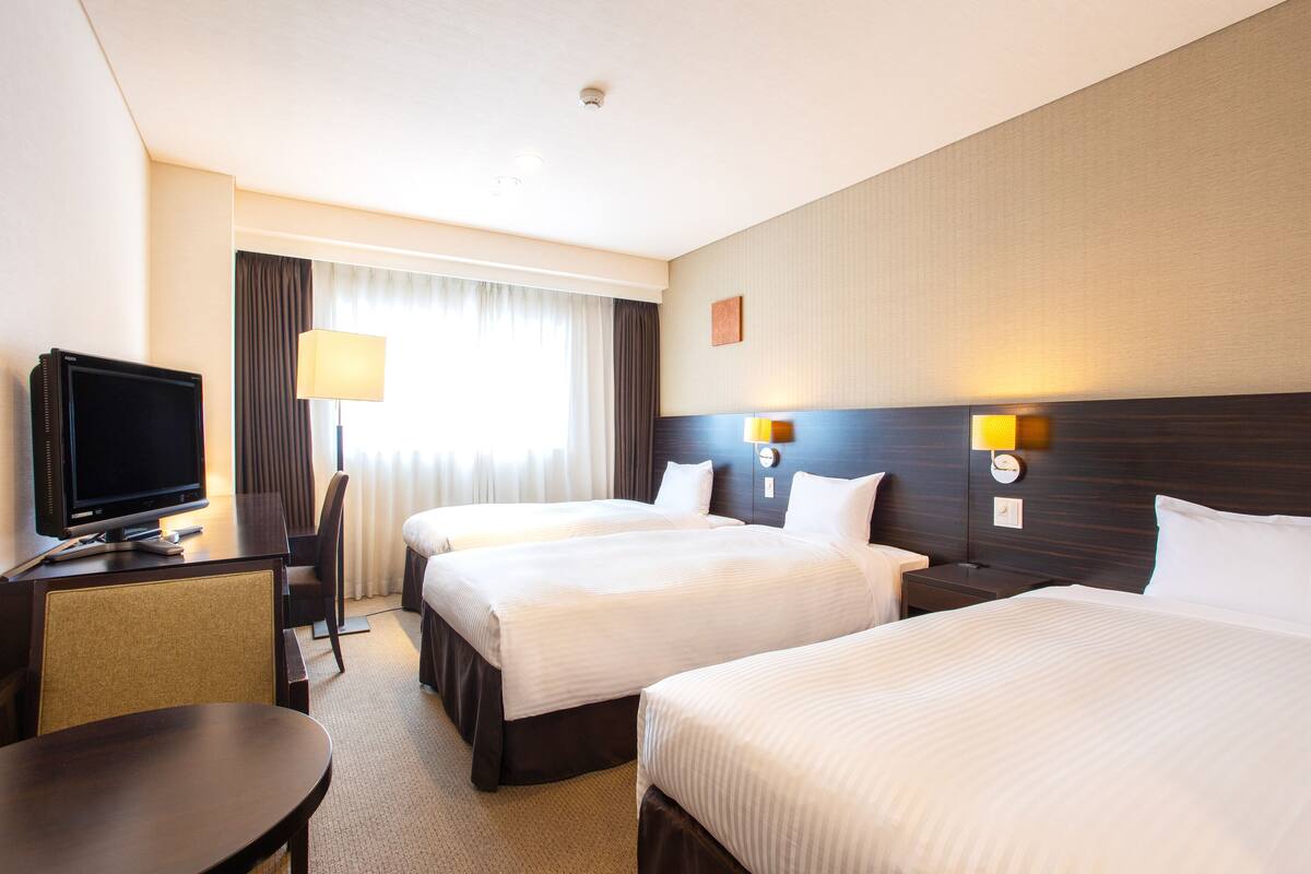 A hotel room with two beds, a desk with a TV, a chair, and a lamp.