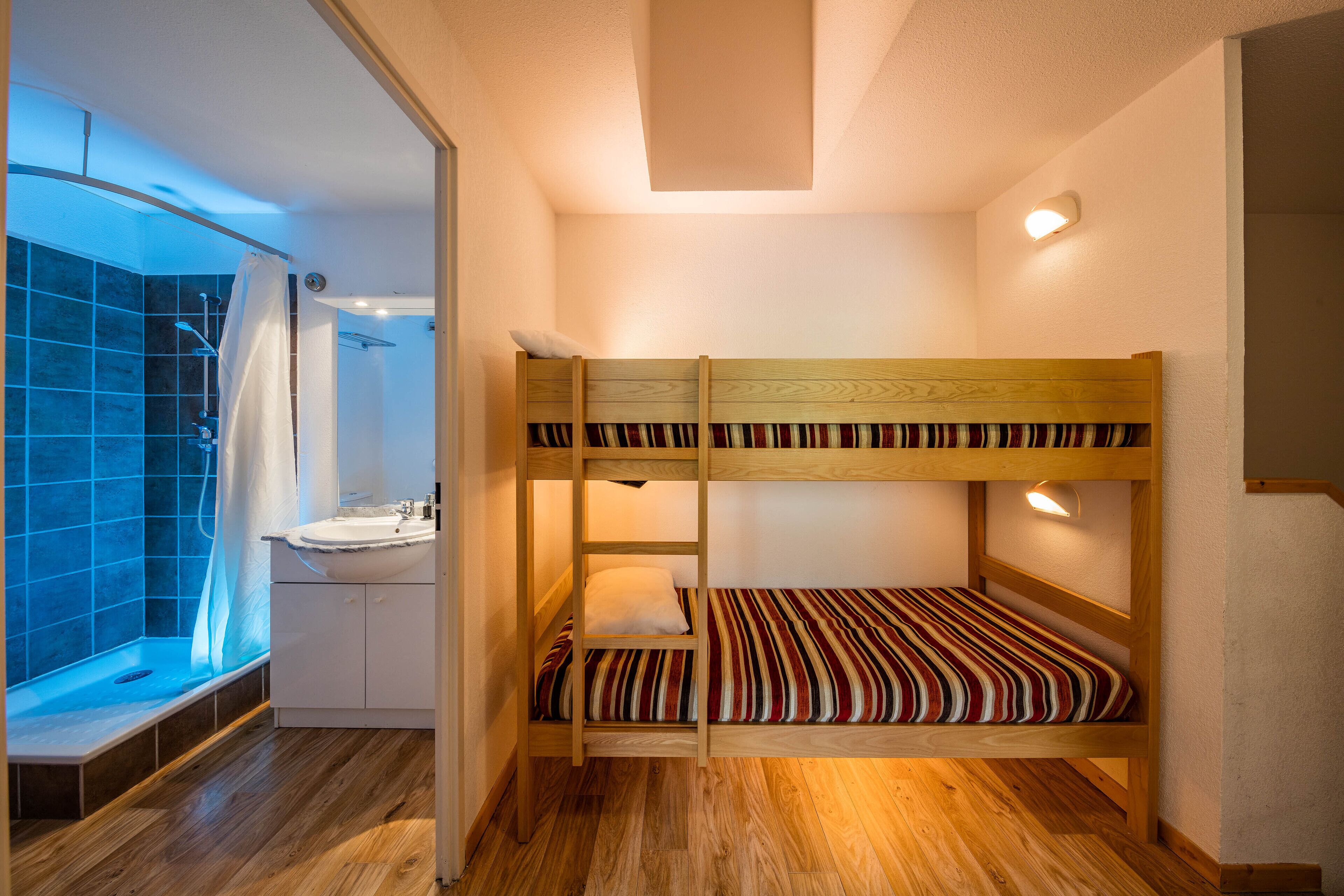 A bunk bed room with a wooden floor, a small sink, and a shower area.