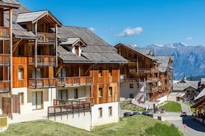 A wooden chalet-style building with balconies and a mountain backdrop. - Noemys Les Chalets de Bois Méan (Les Orres)