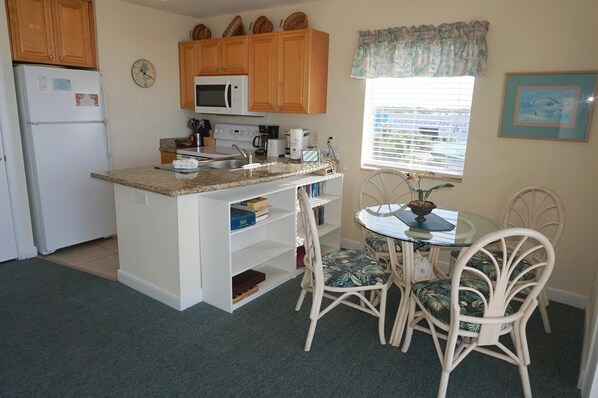 A compact kitchen with wooden cabinets, a microwave, a sink, and a dining area with a glass table and chairs.