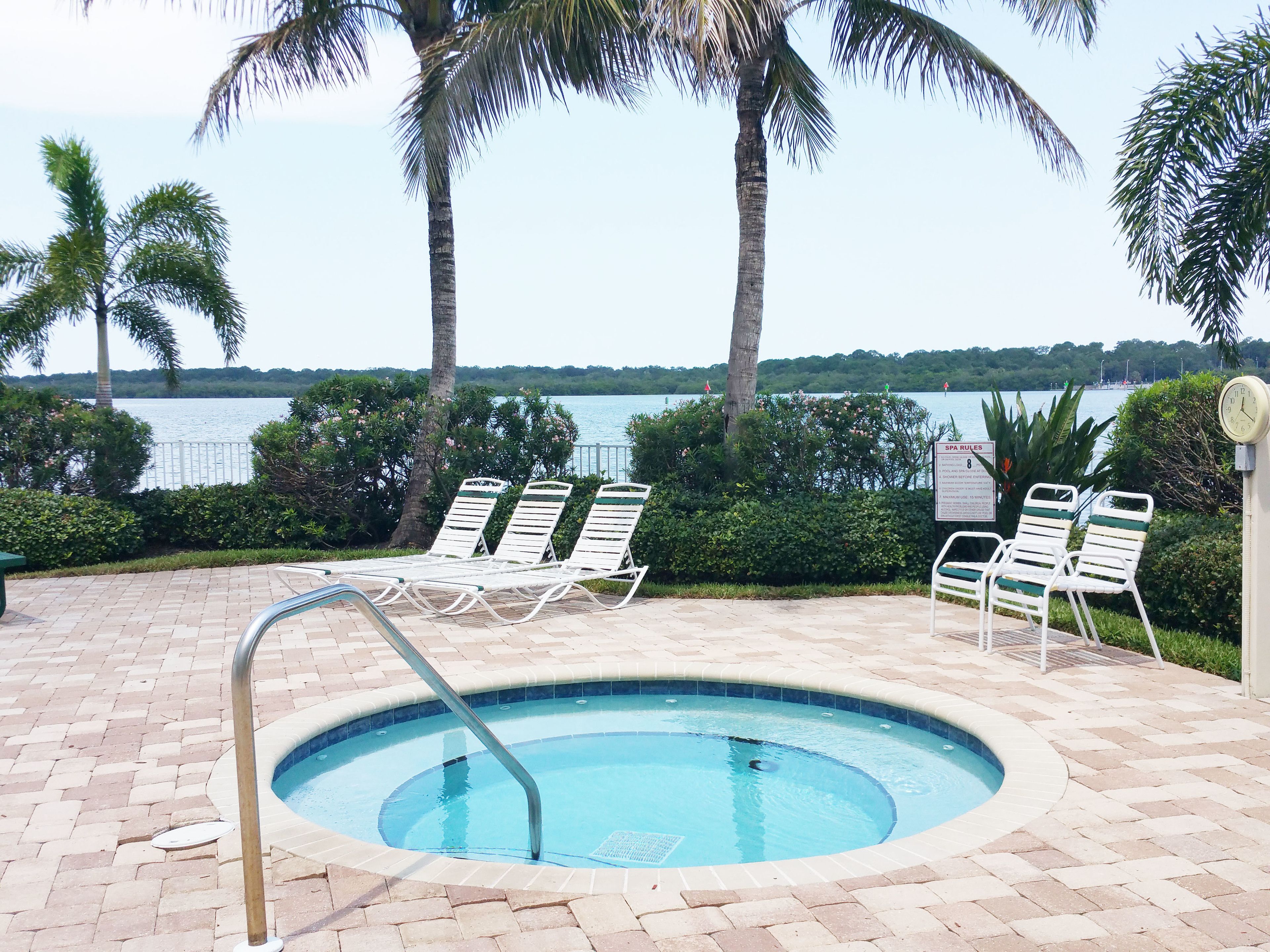 A swimming pool with lounge chairs, palm trees, and a view of the water.