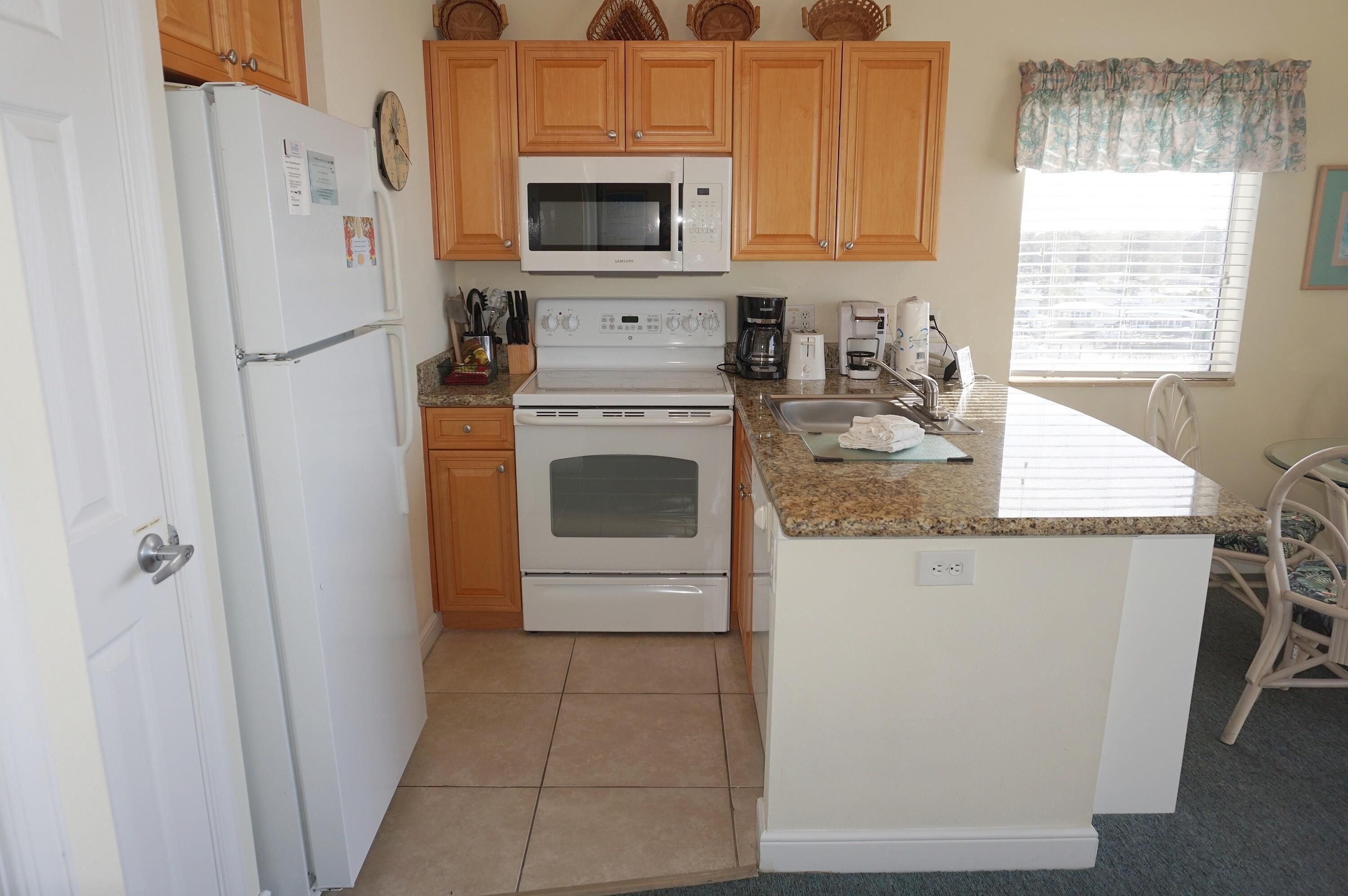 A compact kitchen with wooden cabinets, a microwave, a stove, and a coffee maker.