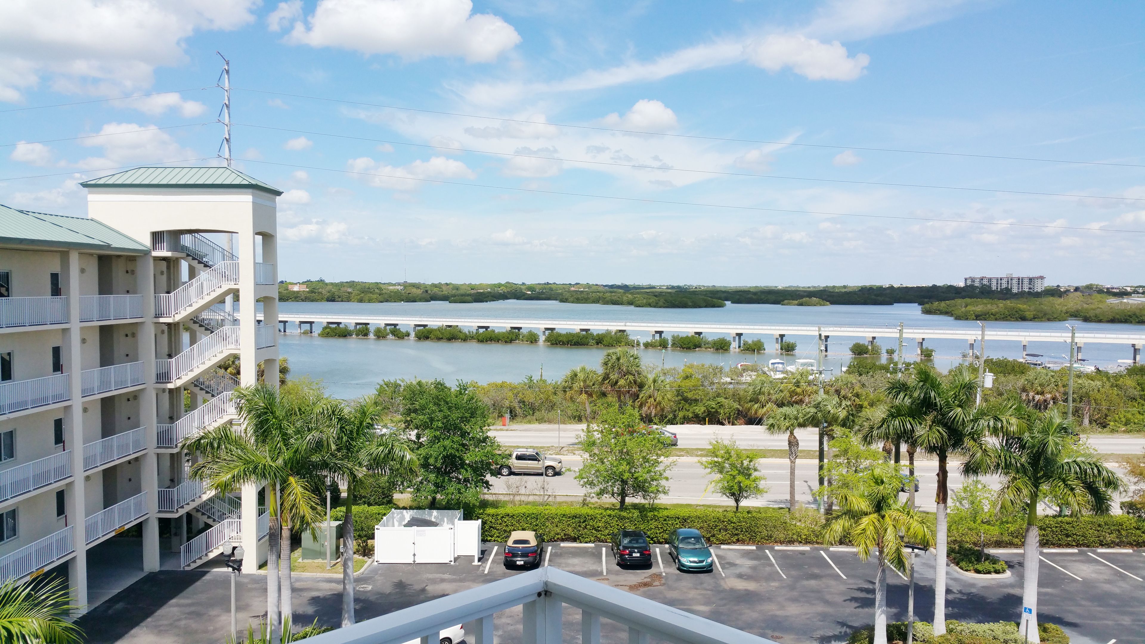 Um hotel com vista para uma ponte sobre a água, estacionamento e palmeiras.