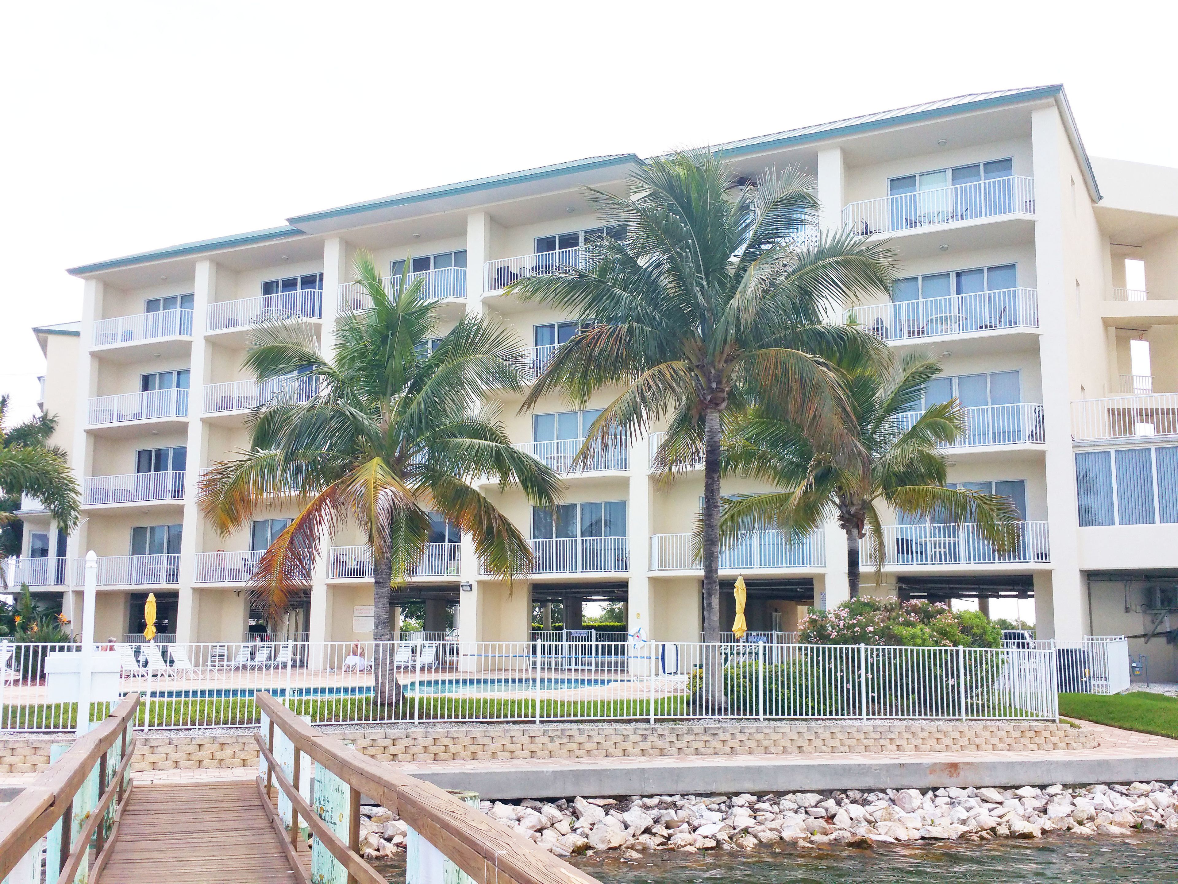 A multi-story hotel with balconies, a pool area, and palm trees.