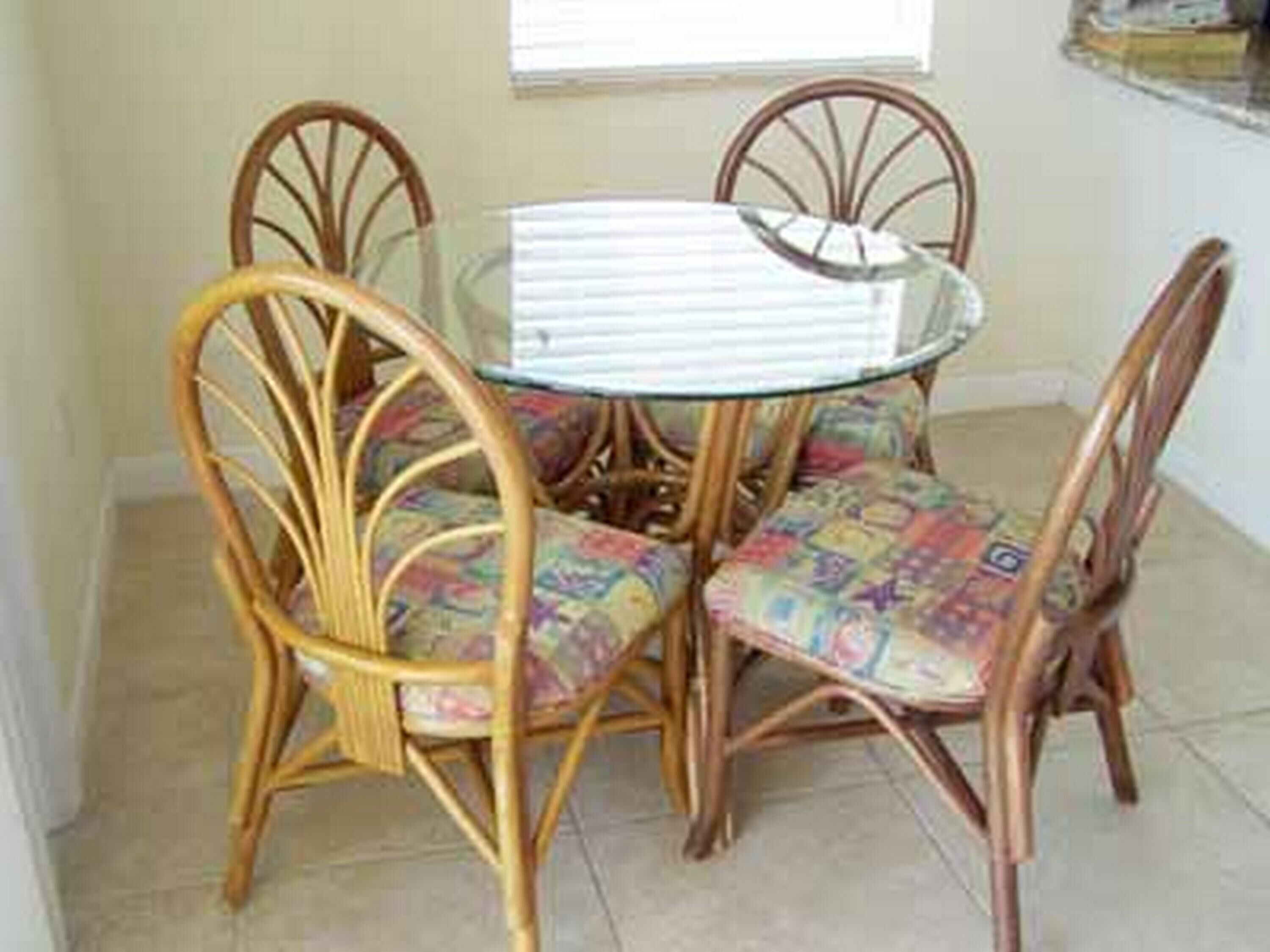 A dining area with a glass-top table surrounded by wicker chairs with colorful cushions.