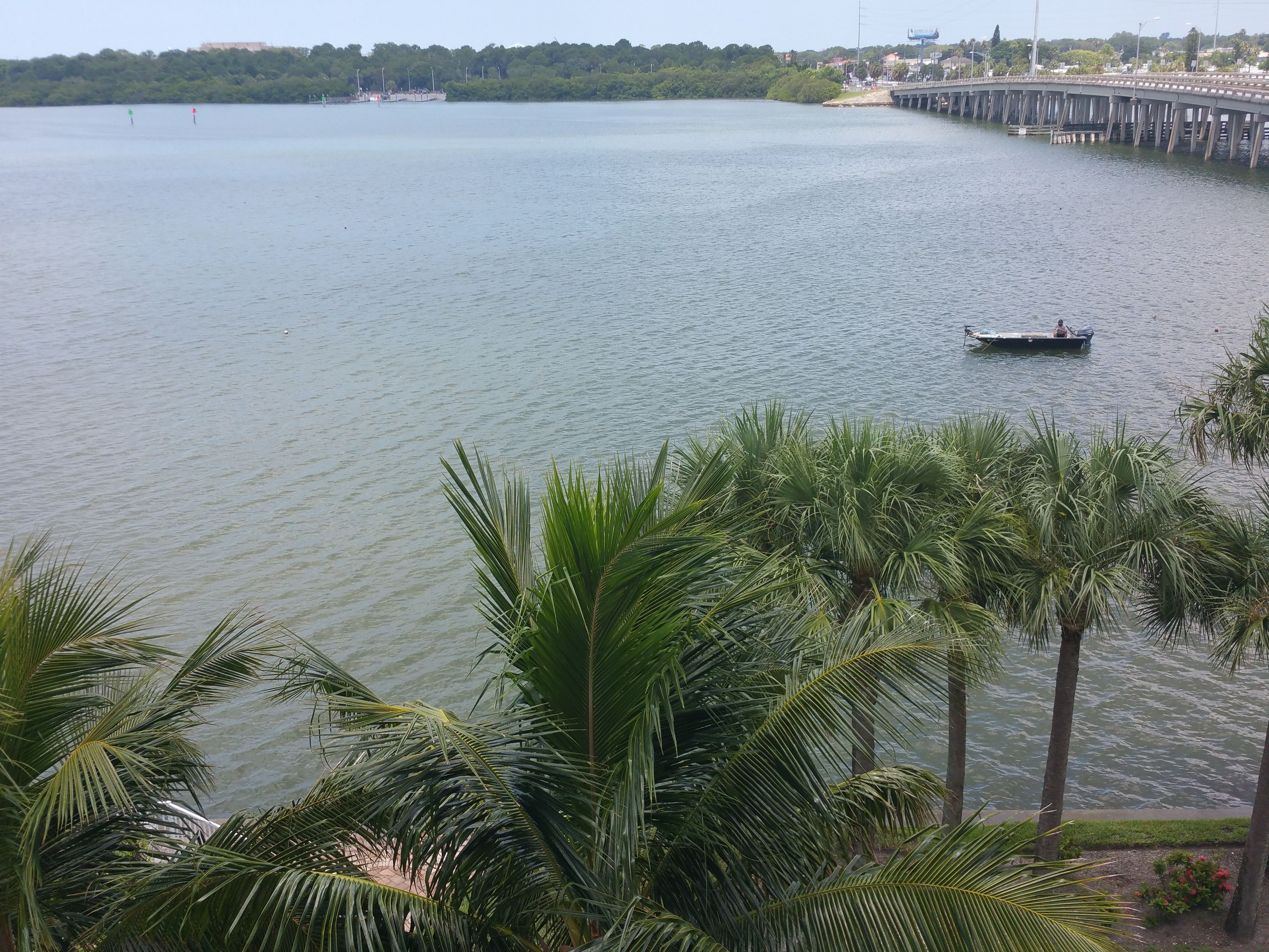 A calm lake with a boat in the distance, surrounded by lush greenery and a bridge.