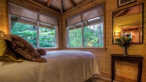 A wooden cabin bedroom with a bed, large windows, and a mirror on the wall.