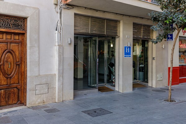 A building entrance with a wooden door, glass doors, and a blue handicap accessibility sign. -  HA Hotel Trebol (Málaga)
