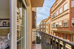 Una calle estrecha flanqueada por edificios, un balcón con baranda metálica y vista a la calle.