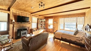 A cozy log cabin room with a fireplace, a television, a bed, a rocking chair, and a bookshelf. - Brewster Inn (Dexter)