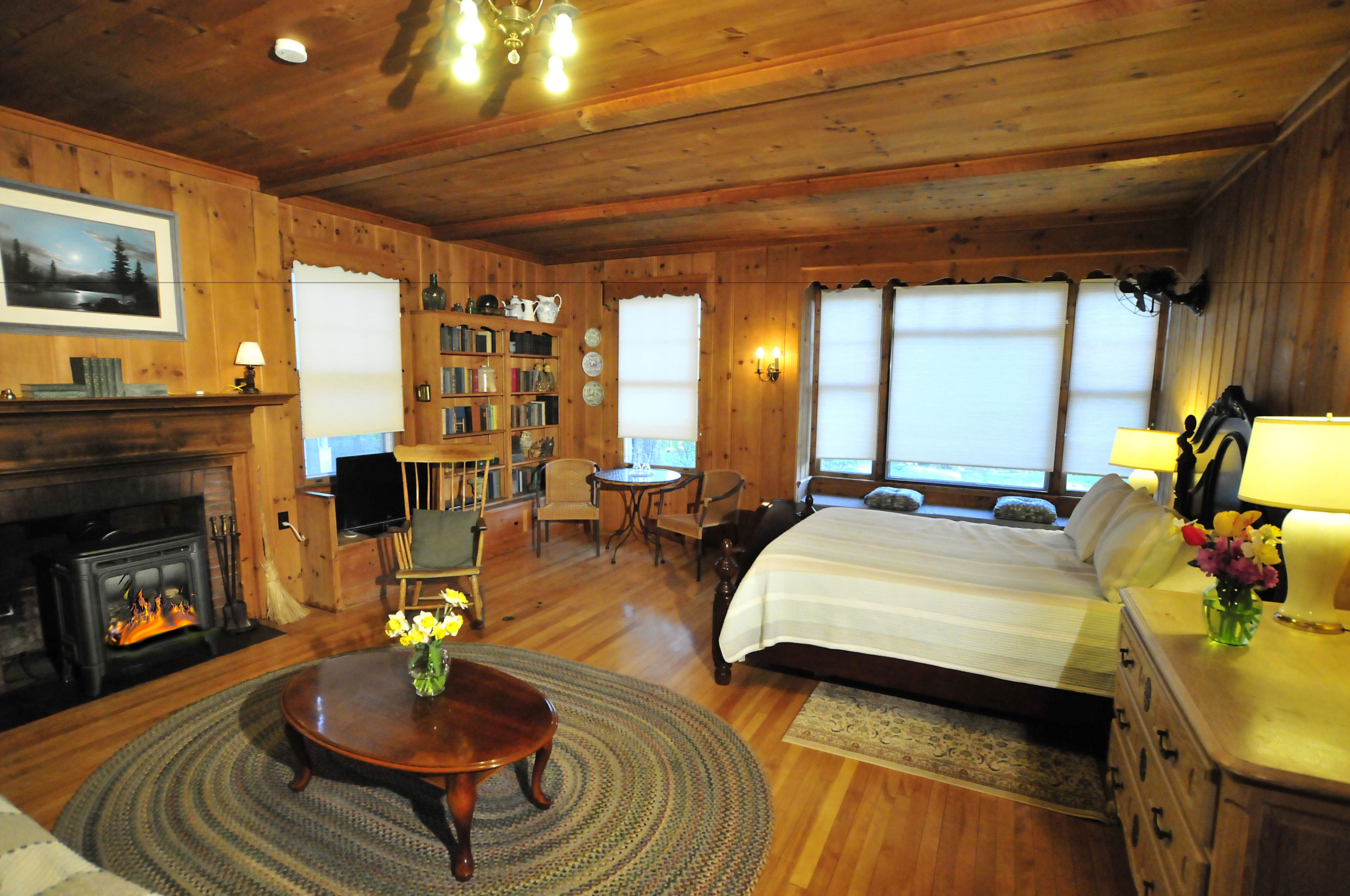 Una acogedora habitación de estilo cabaña de madera con chimenea, una cama grande, una estantería y un comedor.