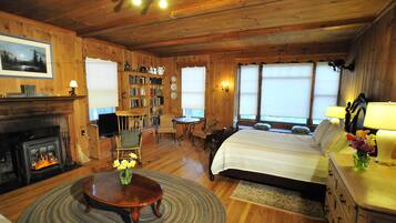 Una acogedora habitación de estilo cabaña de madera con chimenea, una cama grande, una estantería y un comedor.