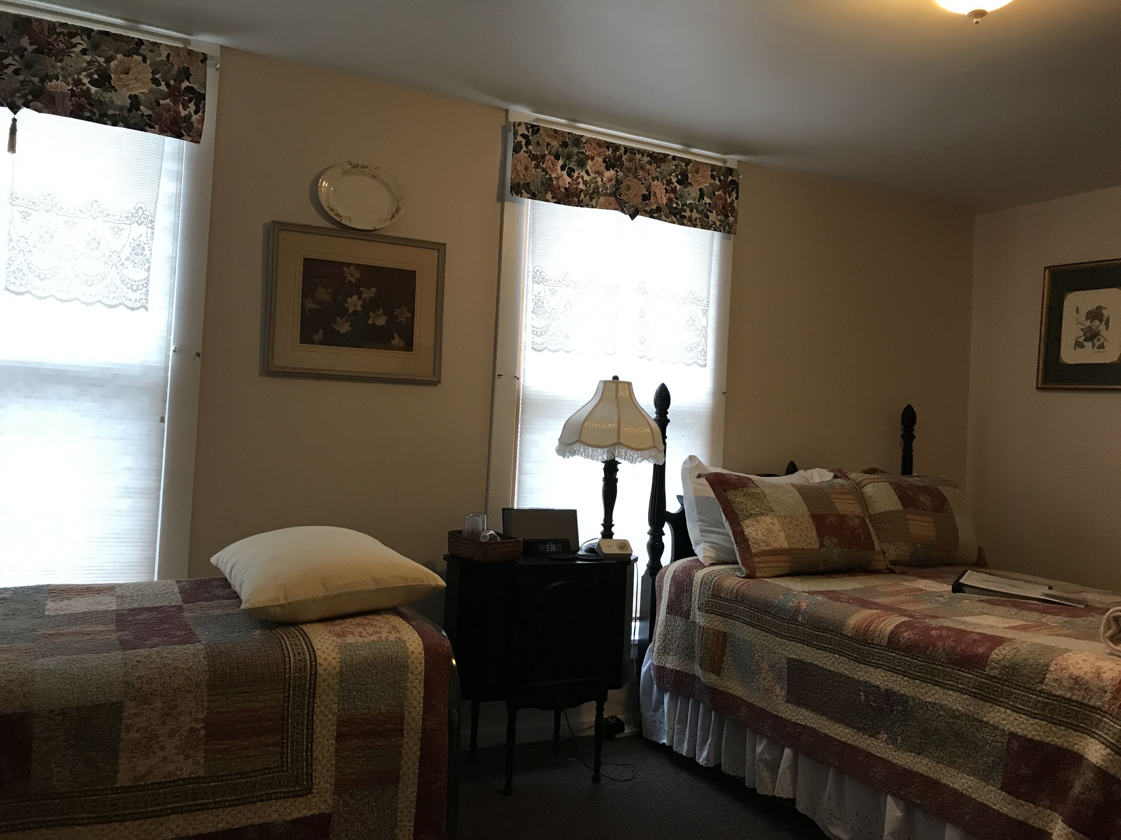 Une chambre avec deux lits, un bureau, une lampe et une fenêtre ornée de rideaux à motifs floraux.