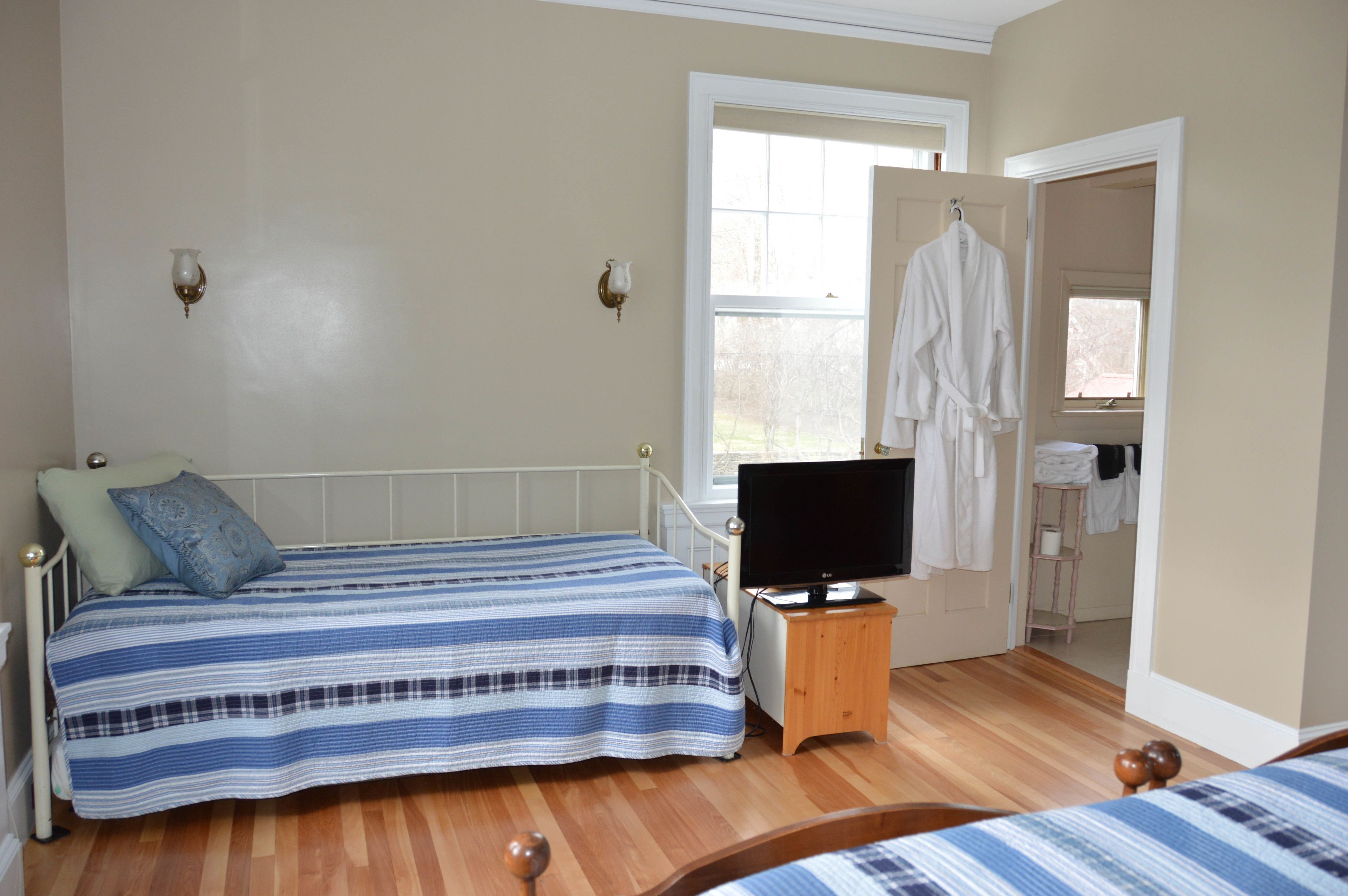 A bedroom with two beds, a TV on a wooden stand, a window, and a door leading to a bathroom.