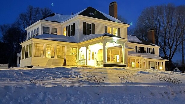 A large, two-story house with a covered front porch and a chimney. - Brewster Inn (Dexter)