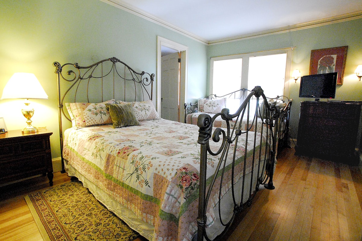 A bedroom with a bed, a nightstand, a dresser, a television, and a window.
